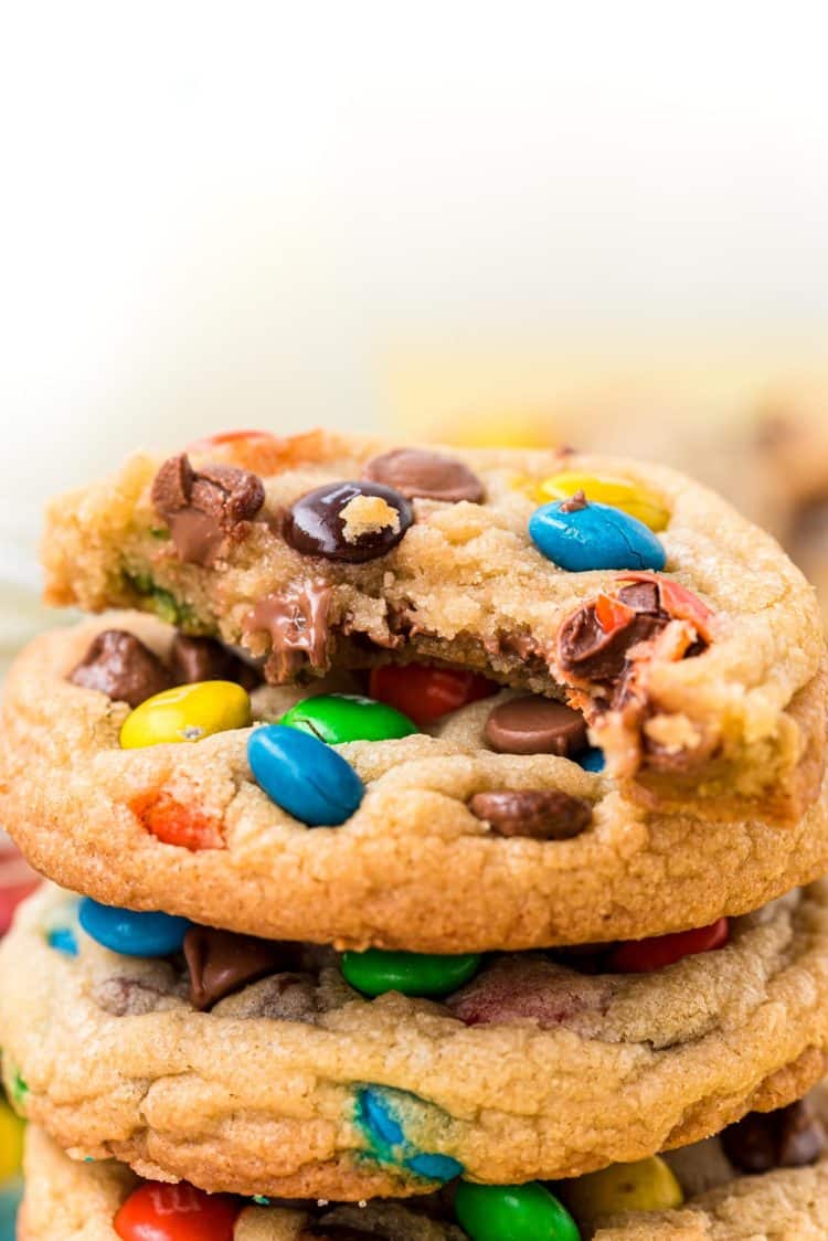 Close up of a stack of M&M cookies with the top one missing a bite.