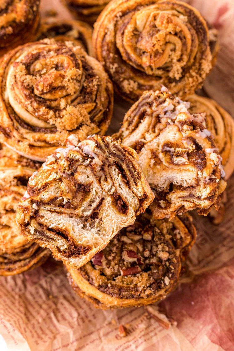 Pumpkin cinnamon rolls muffins piled on top of each other, the top one has been sliced in half to show the inside.