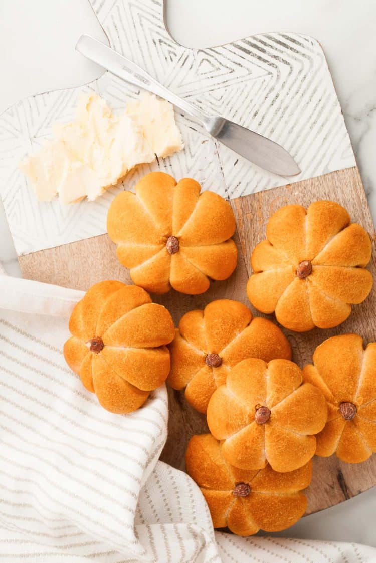 Overhead photo of pumpkin dinner rolls on a serving board with butter.