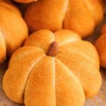 Close up of pumpkin flavored and shaped dinner rolls on a wooden cutting board.