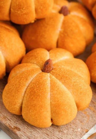 Close up of pumpkin flavored and shaped dinner rolls on a wooden cutting board.