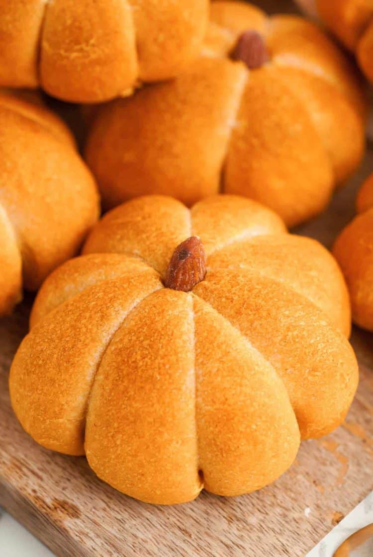 Close up of pumpkin flavored and shaped dinner rolls on a wooden cutting board.