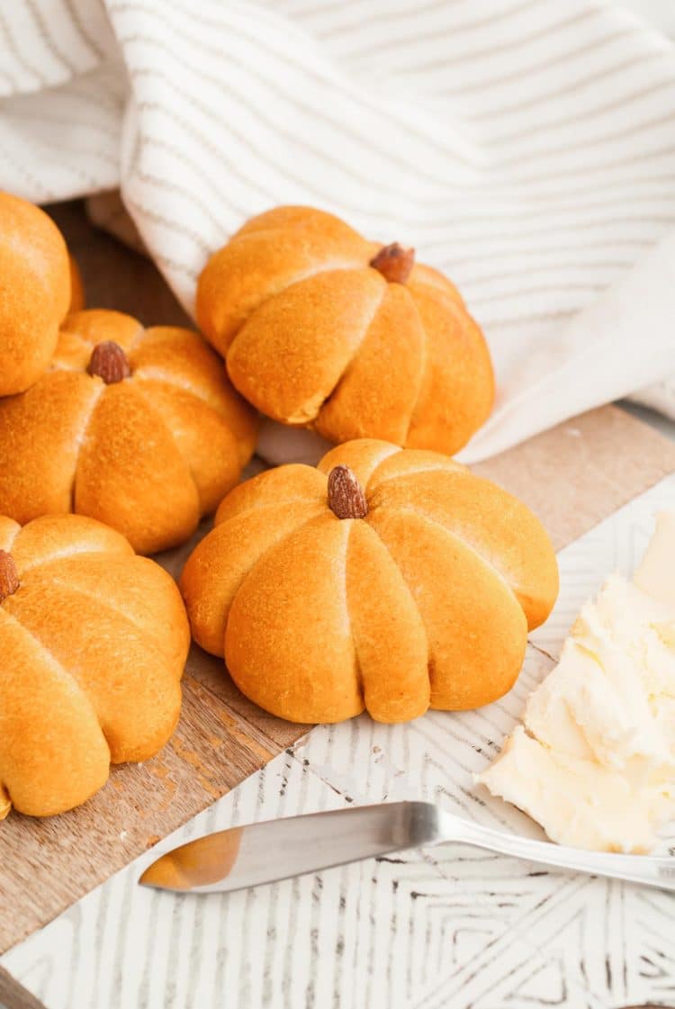 Pumpkin dinner rolls on a seving board with butter and a knife.