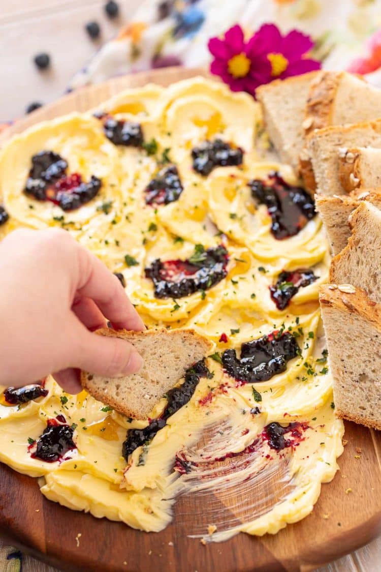 A woman's hand dipping a piece of bread on a butter board.