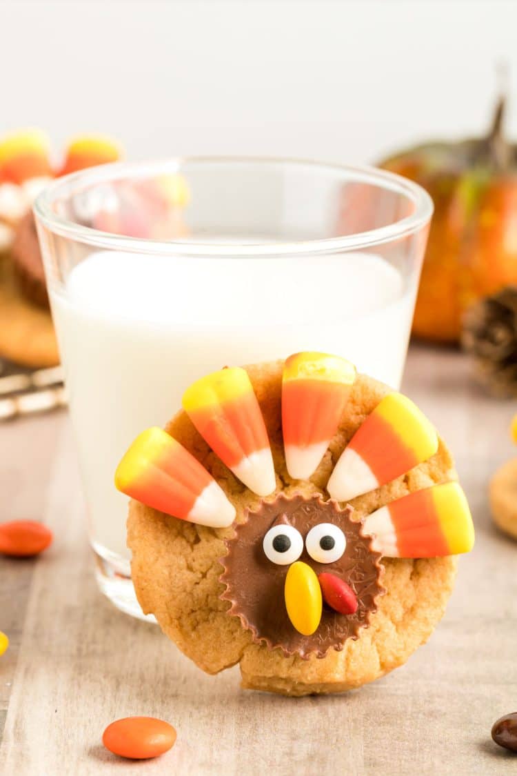 A turkey cookie leaned up against a glass of milk.