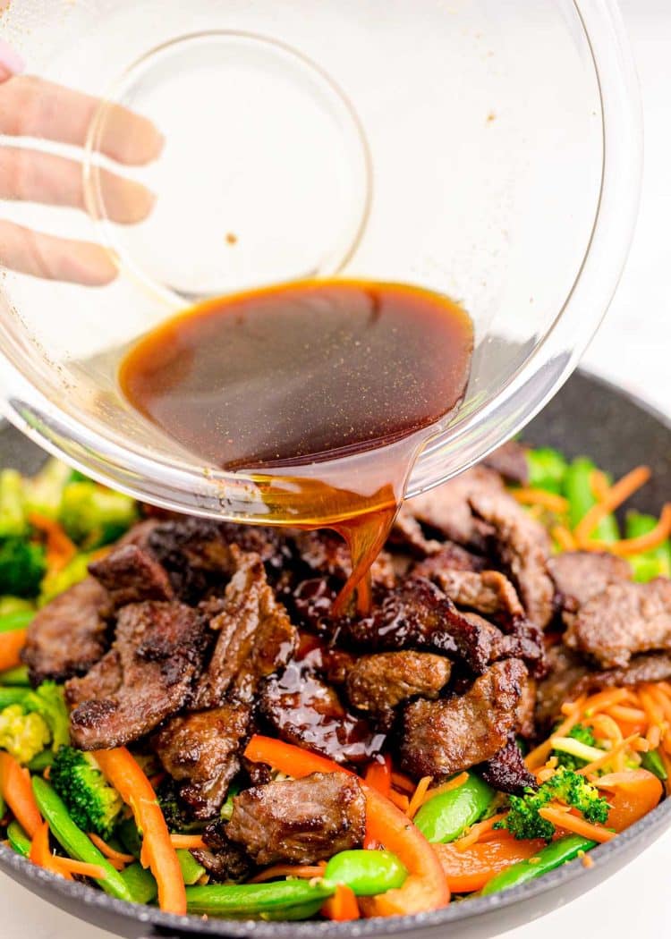 Sauce being poured over beef stir fry in a skillet.