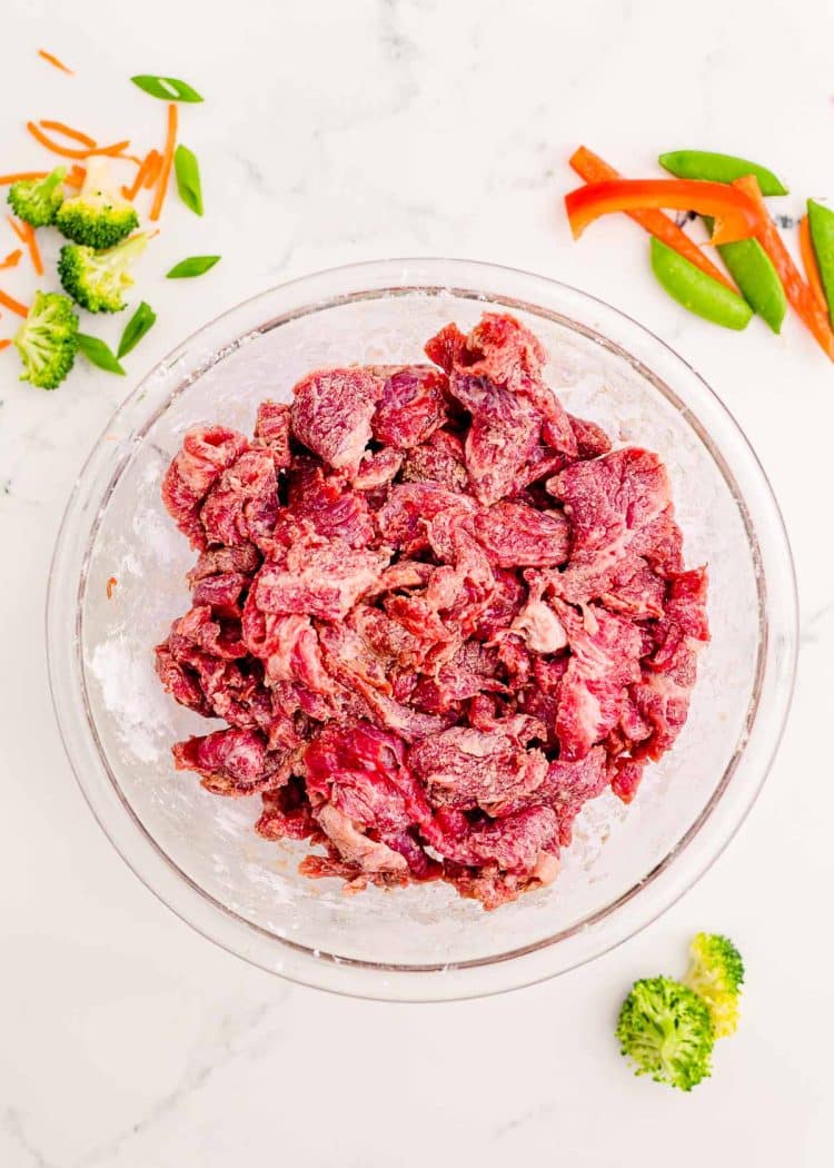 Thin strips of flank steak in a bowl on a marble counter.