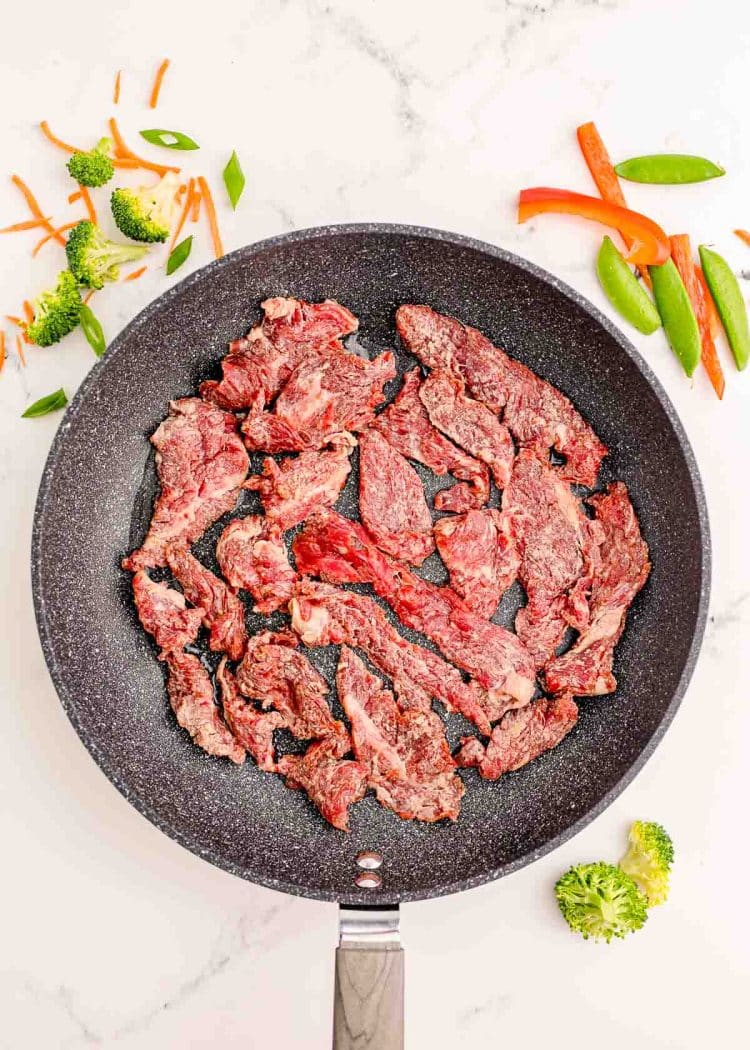 Strips of flank steak being fried in a skillet.