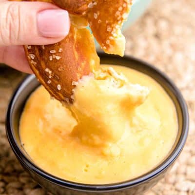 A woman's hand dipping a soft pretzel in beer cheese dip.