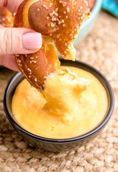 A woman's hand dipping a soft pretzel in beer cheese dip.