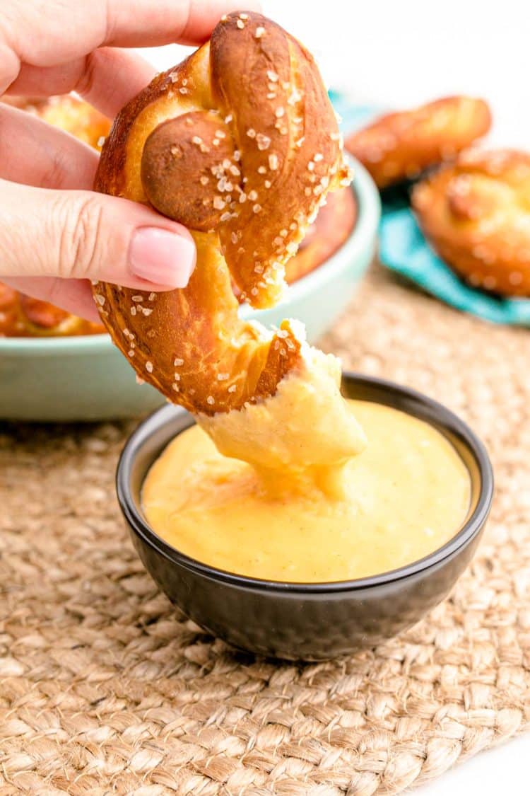 A woman's hand dipping a soft pretzel in beer cheese dip.