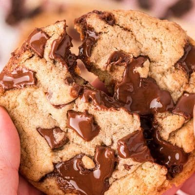 A woman's hand breaking a brown butter chocolate chip cookie in half.