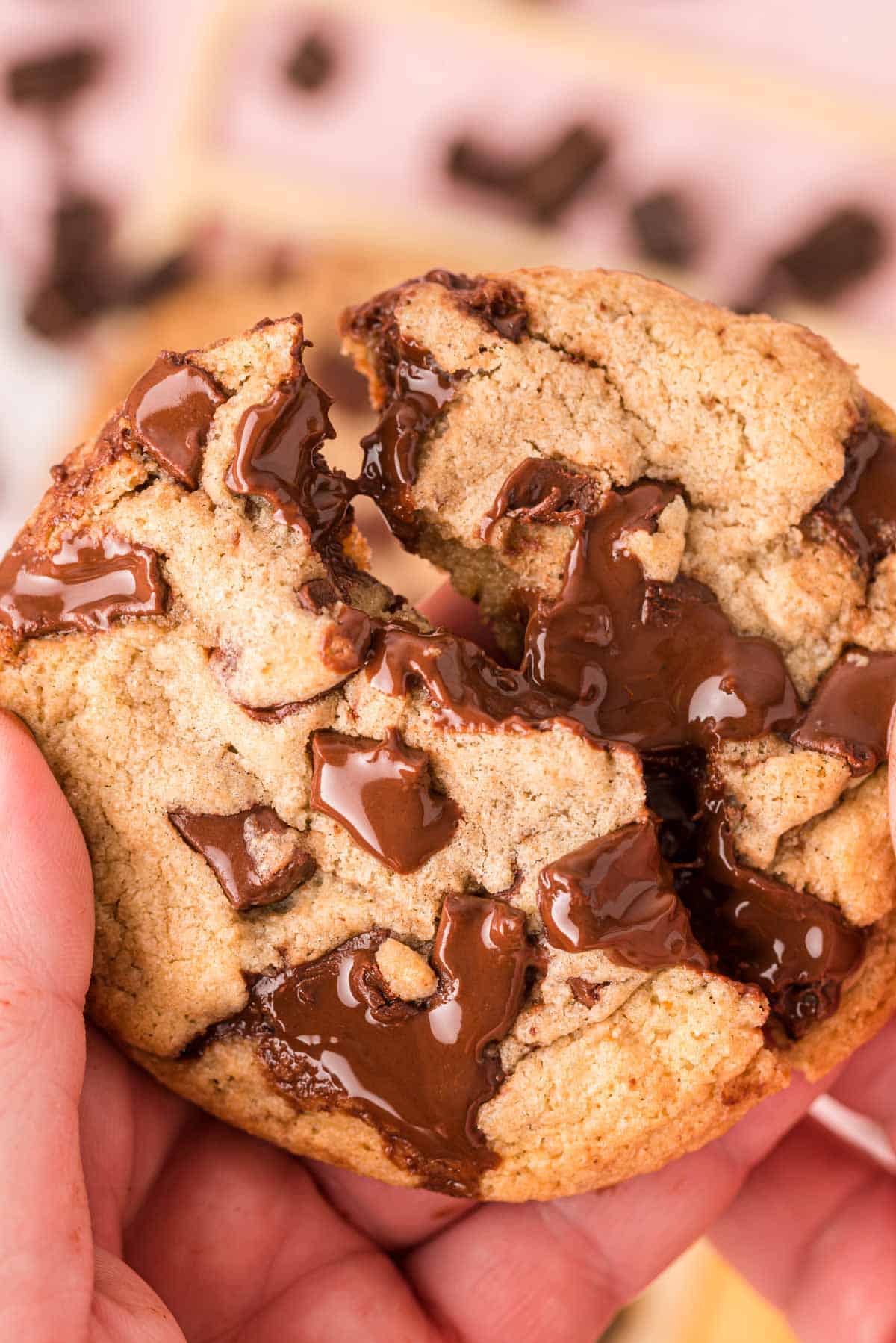 A woman's hand breaking a brown butter chocolate chip cookie in half.