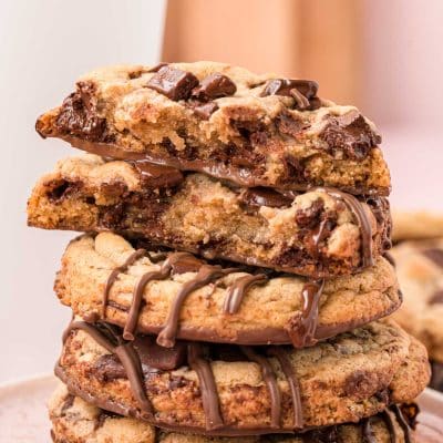 A stack of brown butter chocolate chip cookies on a white plate. The top cookie had been broken in half to show the inside.