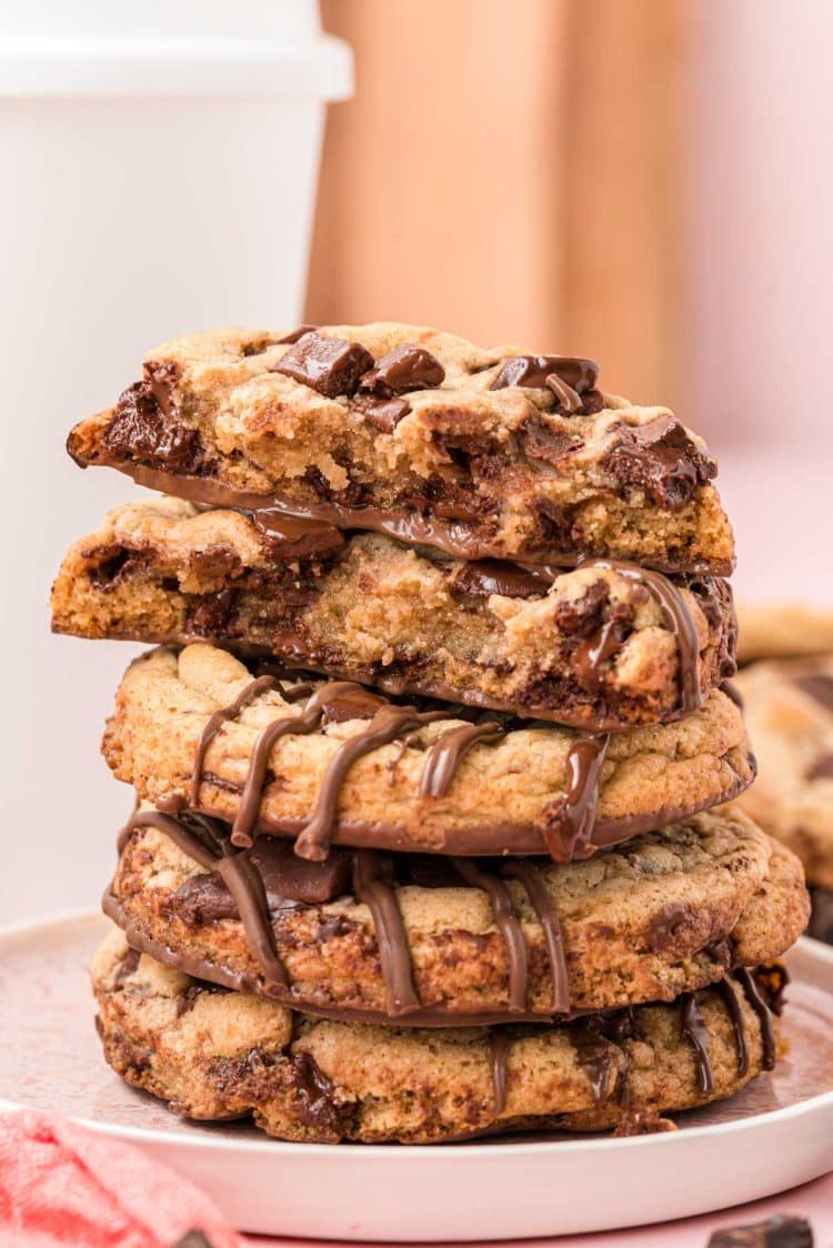 A stack of brown butter chocolate chip cookies on a white plate. The top cookie had been broken in half to show the inside.