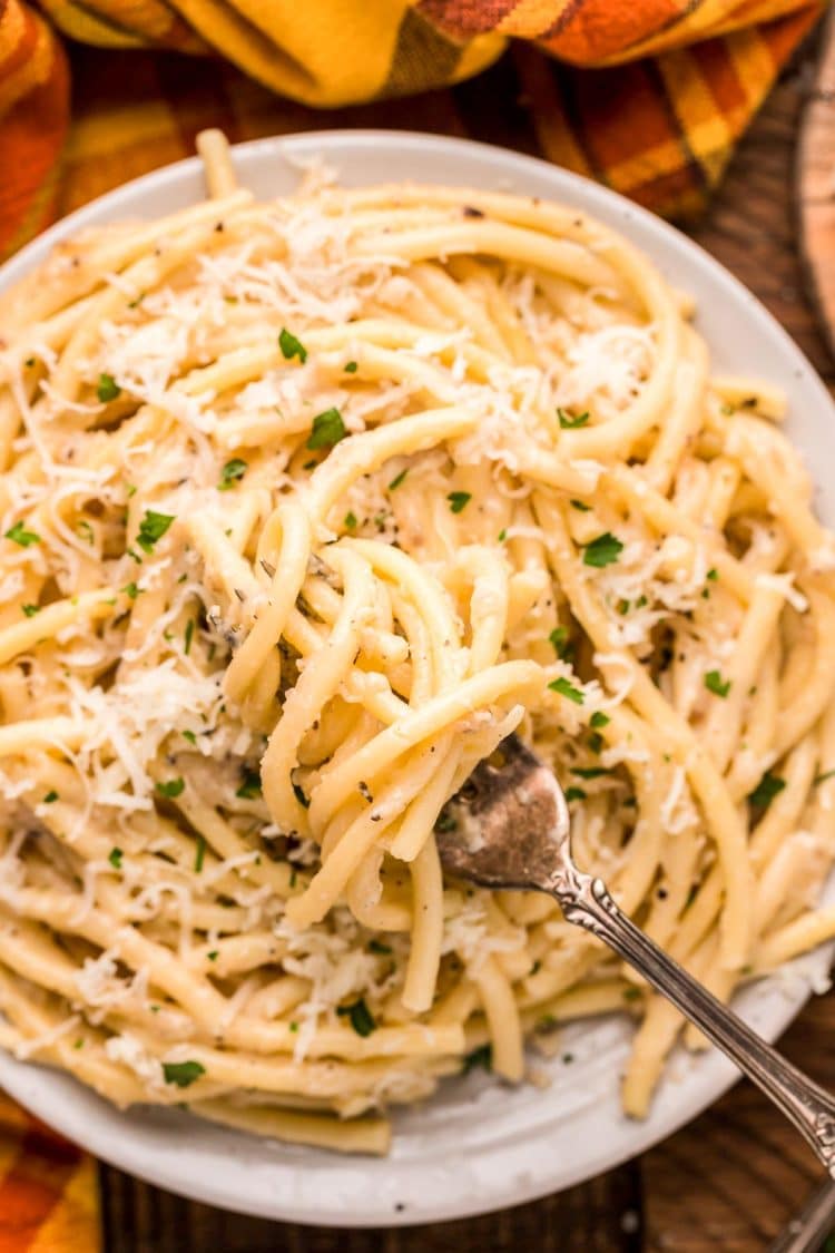 A fork being twirled in a plate of bucatini cacio e pepe.