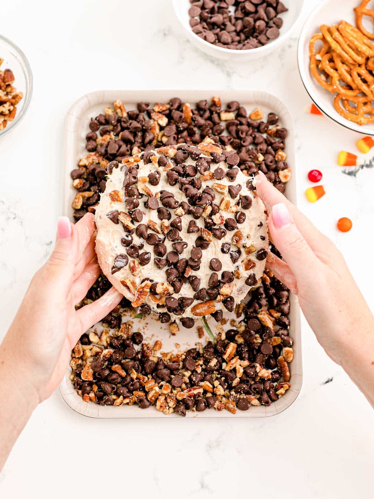 cheese ball being dipped into pecans and chocolate chips.