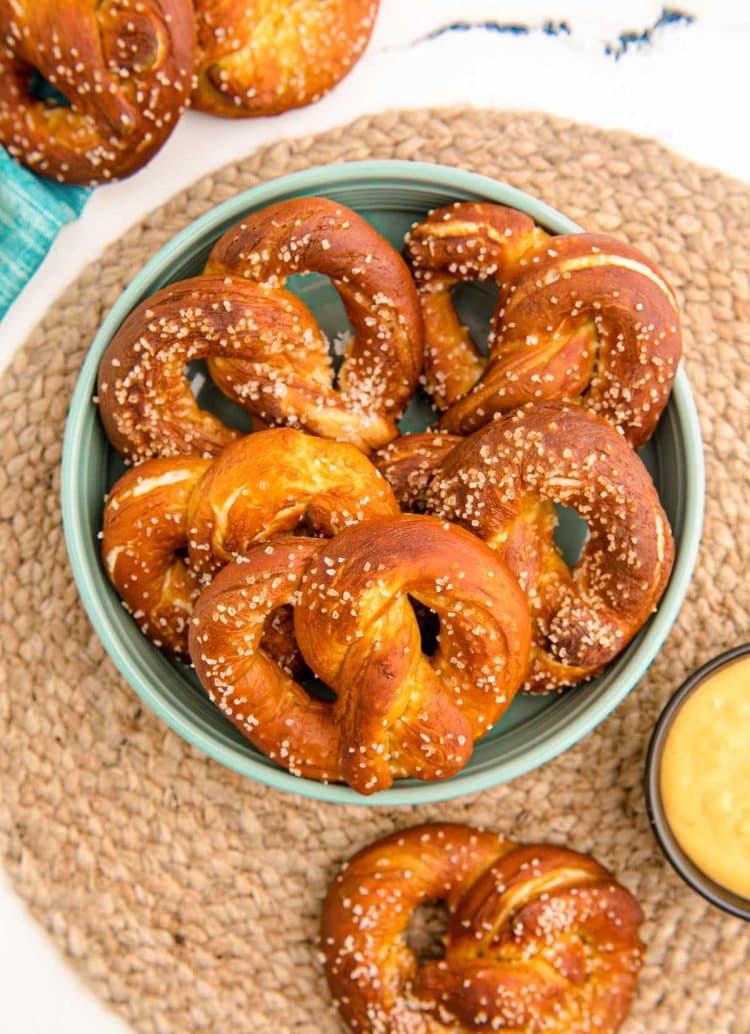 Overhead photo of soft pretzels in a teal bowl on a placemat.