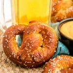 Close up of a soft pretzel leaning against a mug of beer.