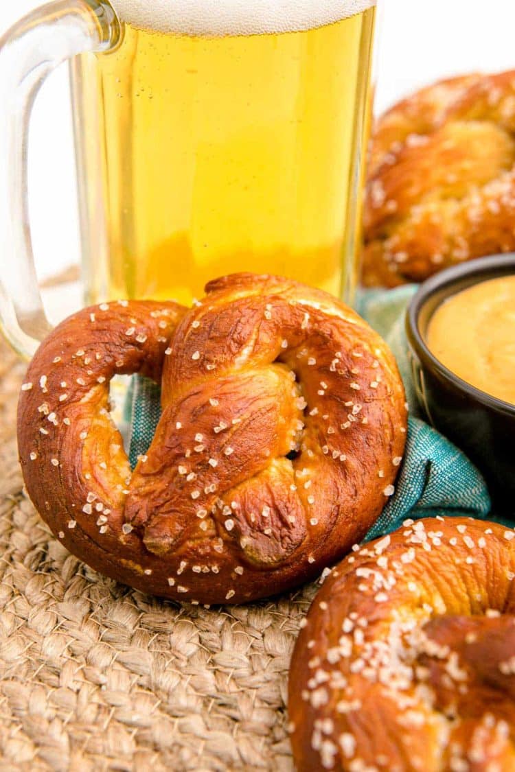 Close up of a soft pretzel leaning against a mug of beer.