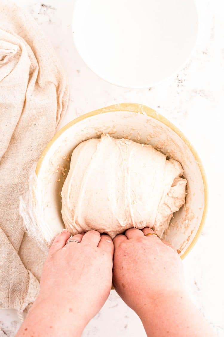 A woman's hand reaching under a ball of sourdough dough in a bowl.