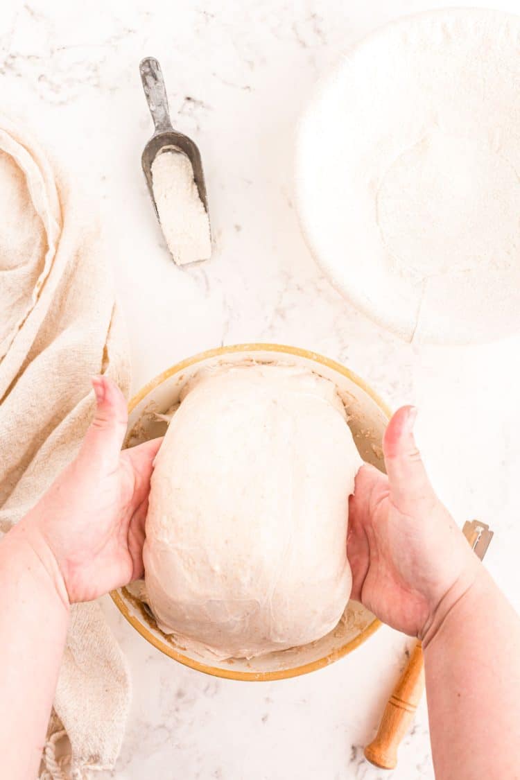 A woman's hands lifting sourdough dough out of a mixing bowl.