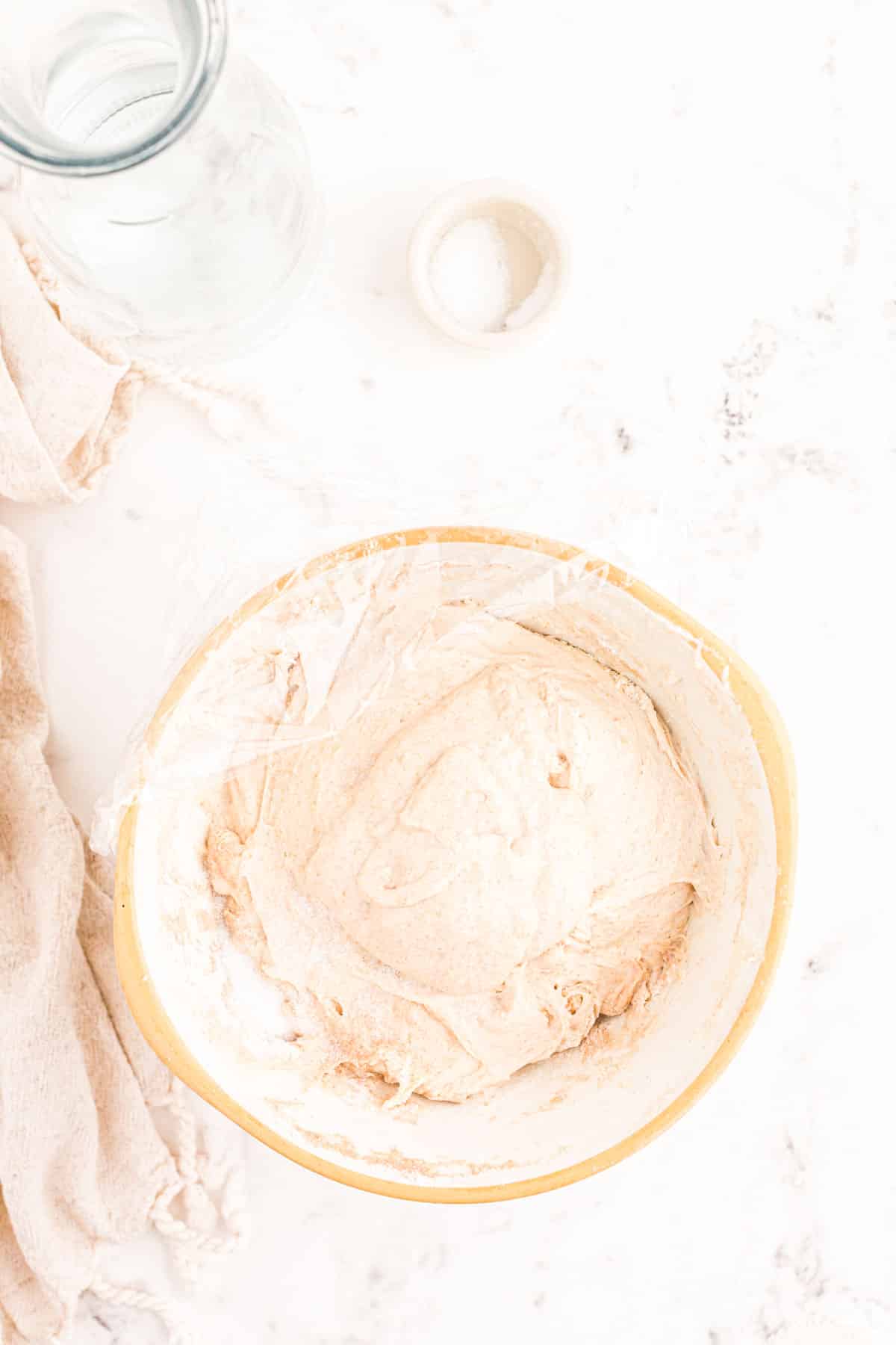 Sourdough dough in a bowl covered in plastic wrap.