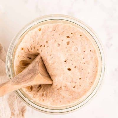 A wooden spoon scooping sourdough starter out of a glass jar.