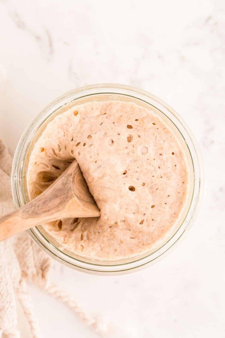 A wooden spoon scooping sourdough starter out of a glass jar.