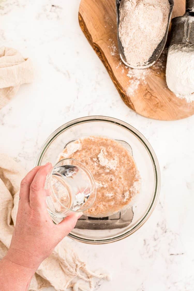 Water being poured into a bowl with flour to make a sourdough starter.