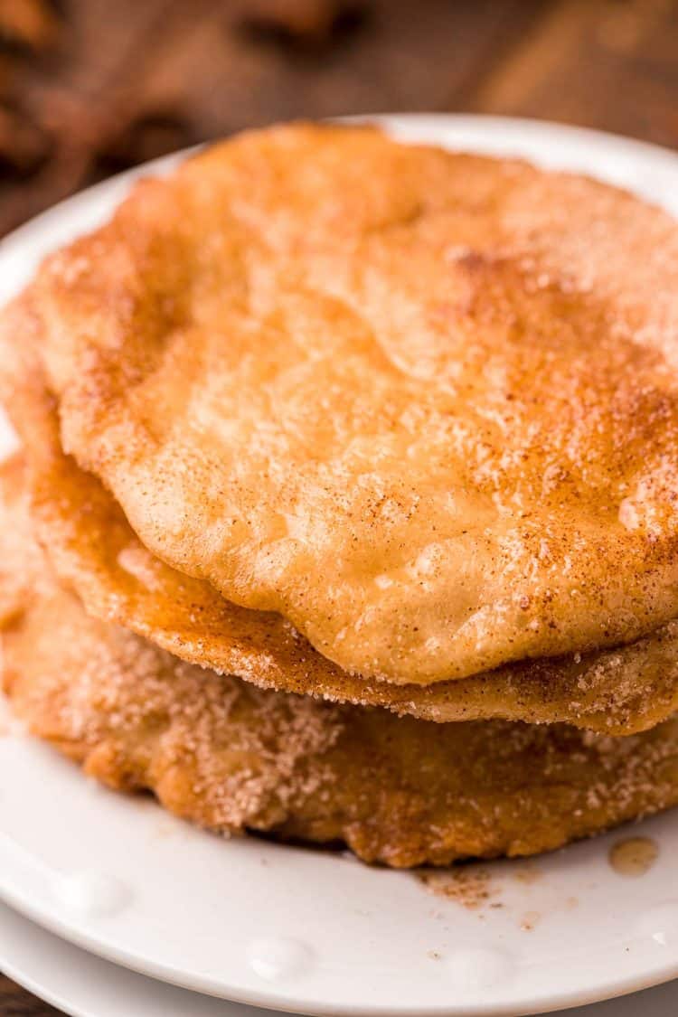 Bunuelos stacked on a white plate that have had syrup poured on them.