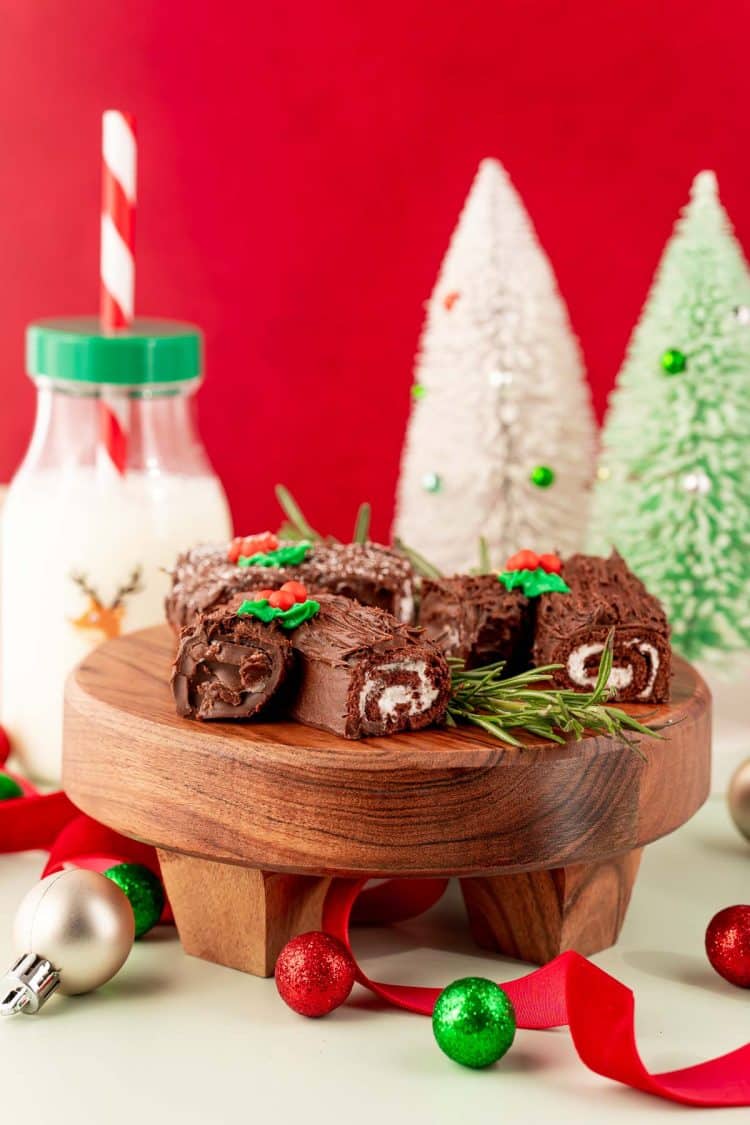 Mini yule log cakes on a cake stand with holiday decorations in the background.