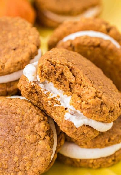 Pumpkin oatmeal cream pies piled on a yellow surface.