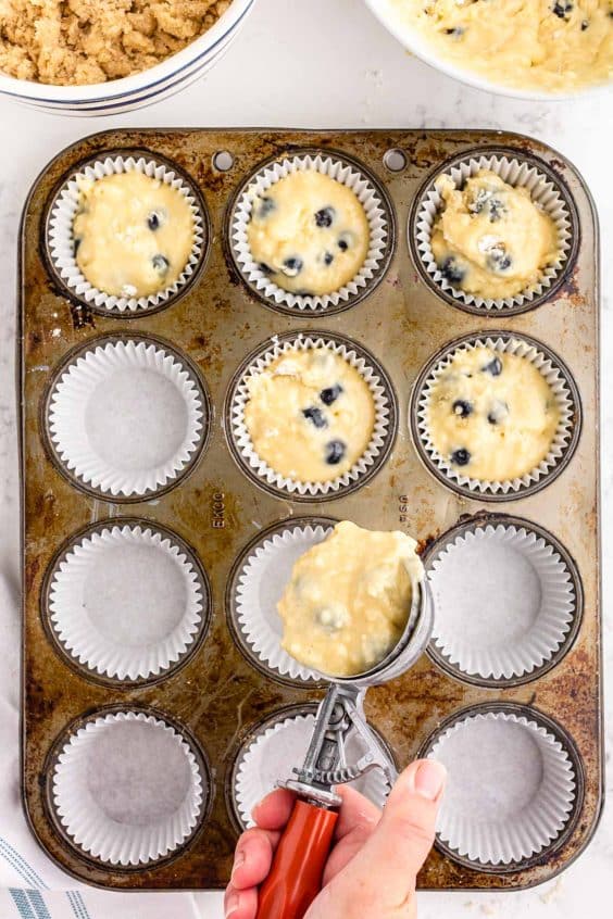 Blueberry muffin batter being scooped into muffin liners.