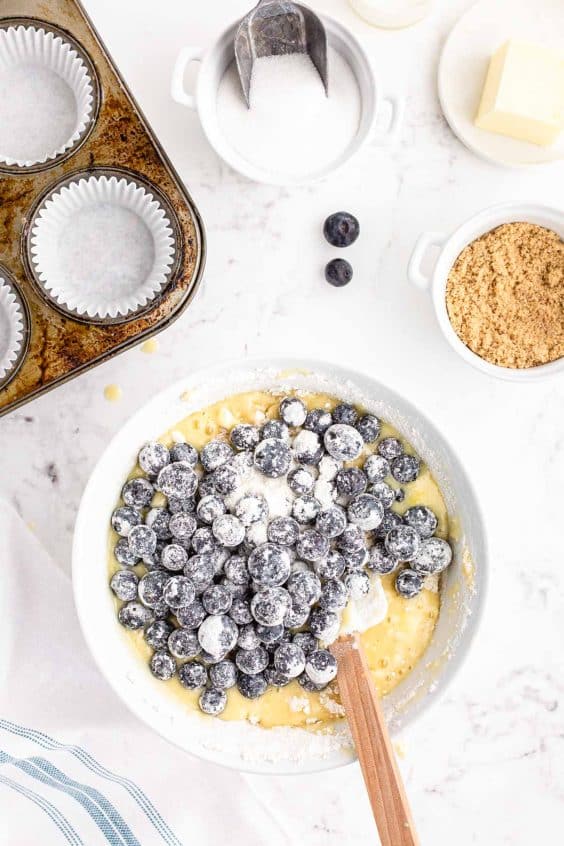 Overhead photo of blueberries coated in flour being added to a mixing bowl with muffin batter.