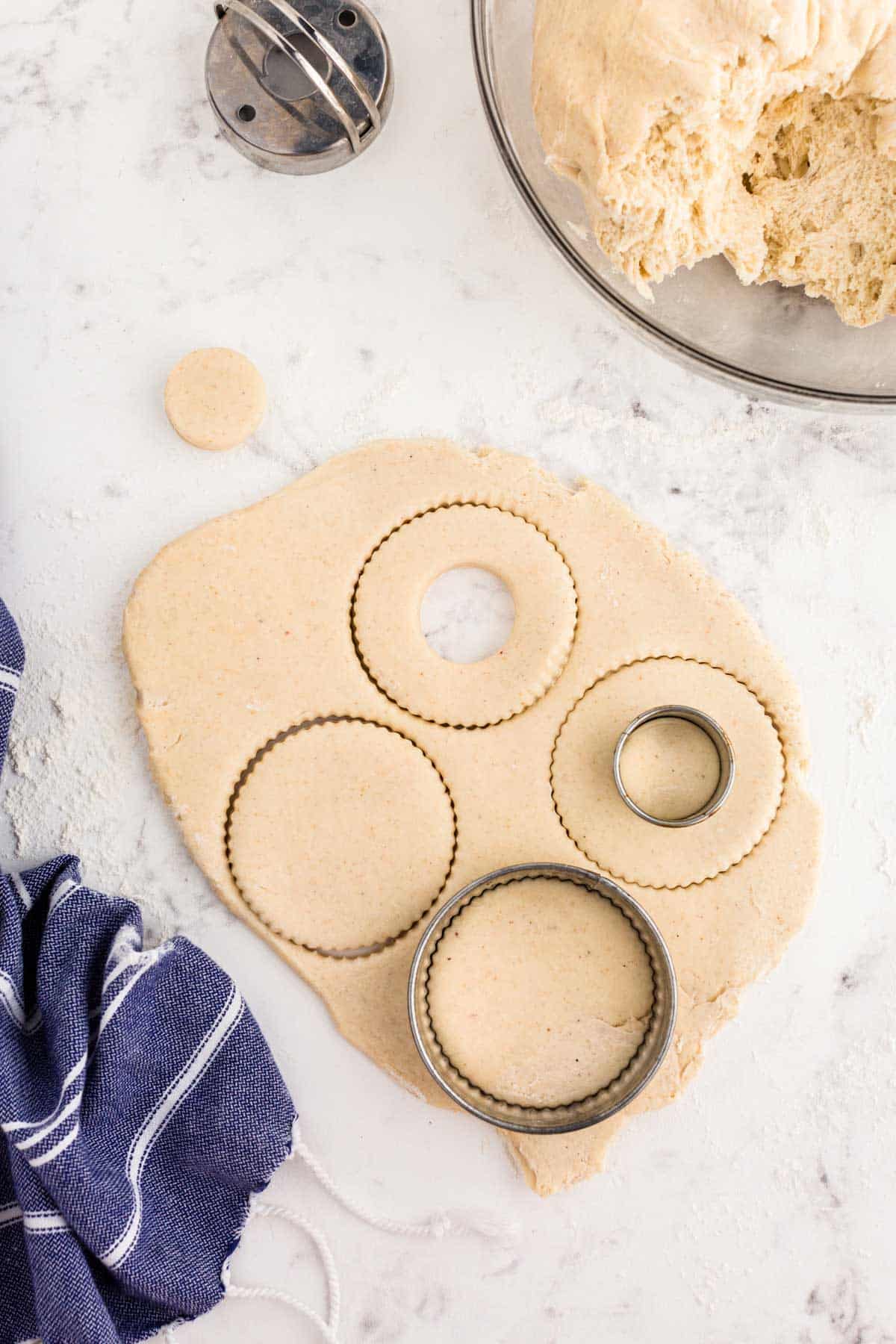 Donuts being cut out of dough with a cutter.