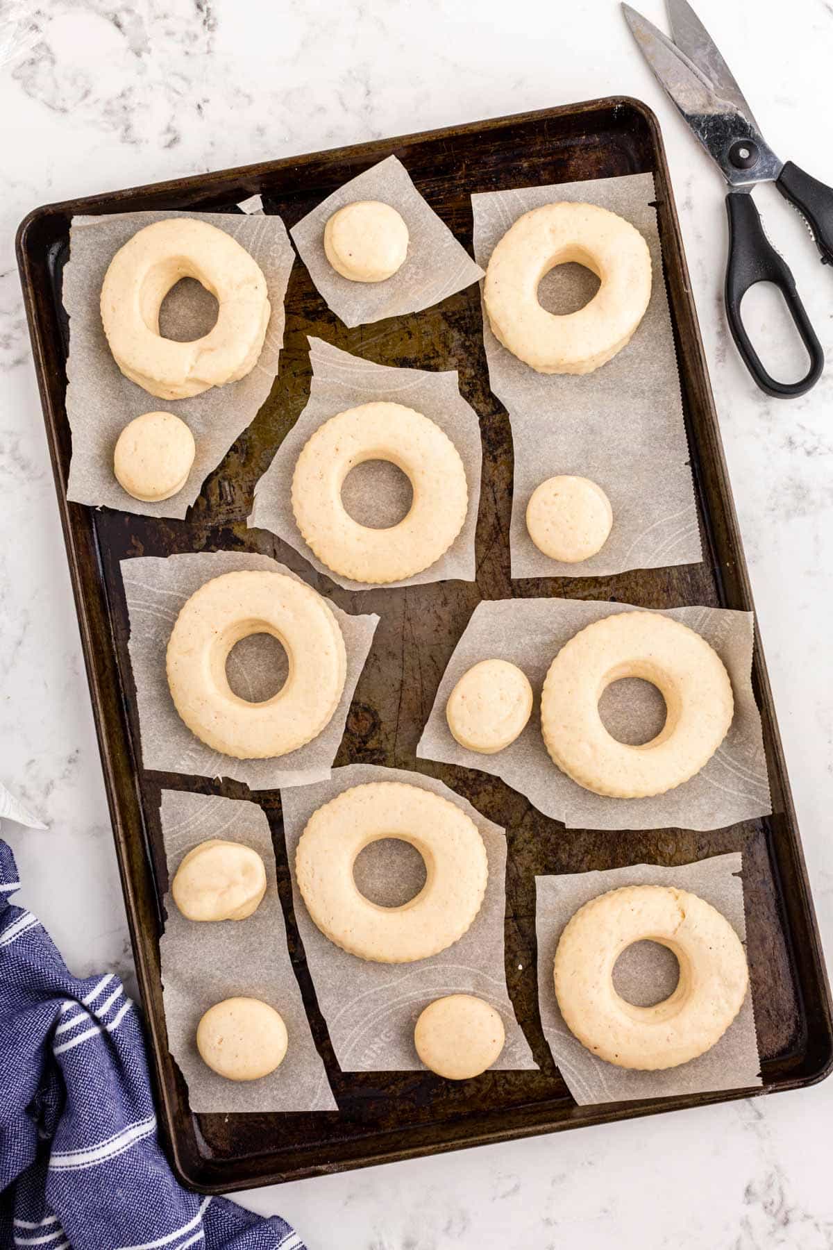 Donuts ready to be fried, resting on a baking sheet.