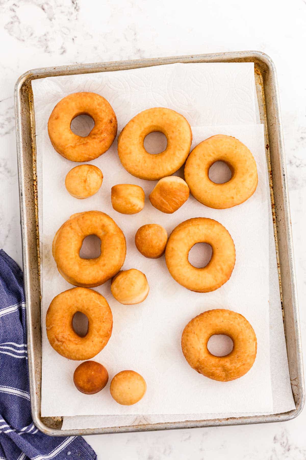 Fried donuts on a paper towel lined baking sheet.