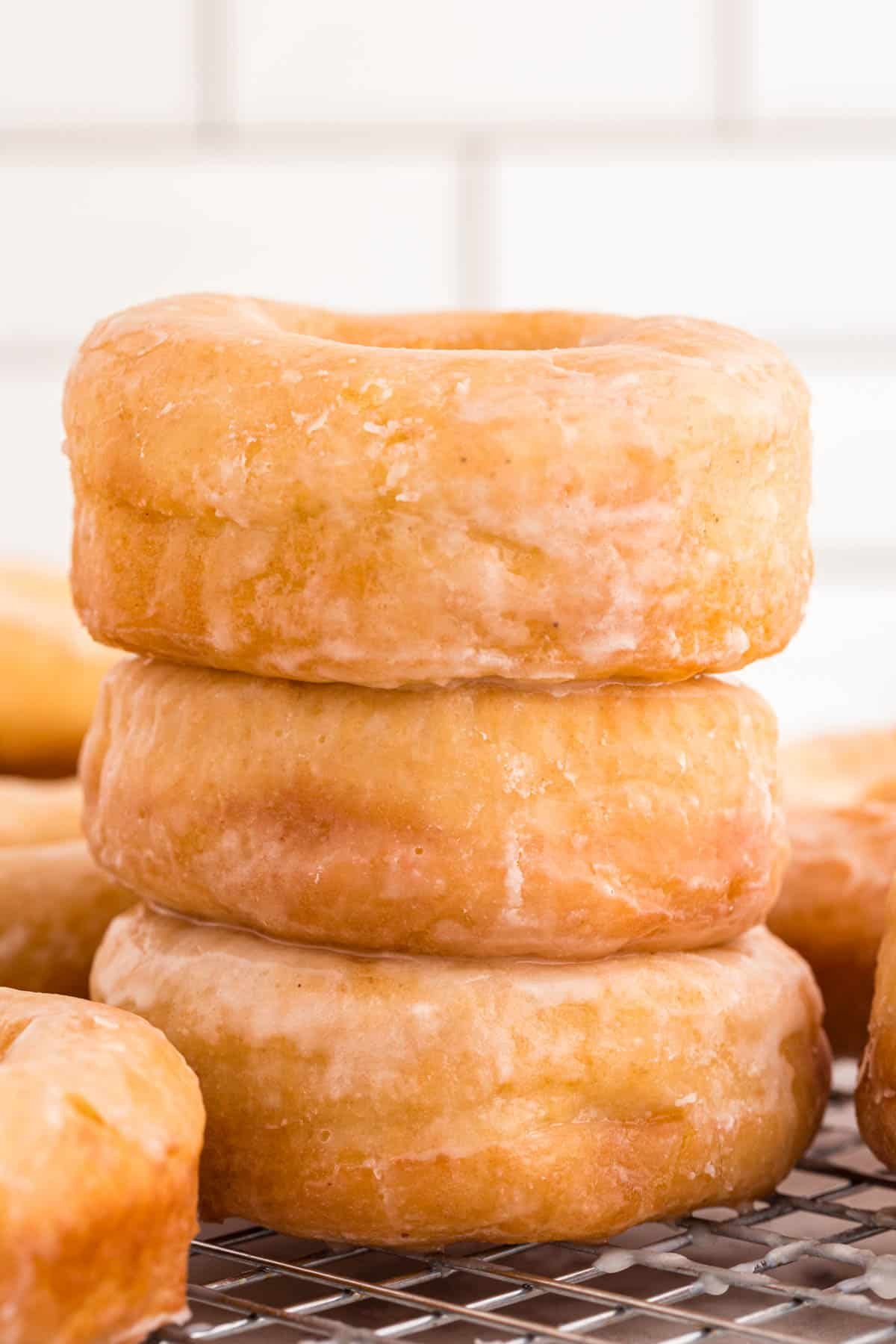 A stack of three glazed donuts on a wire rack.