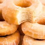 Close up photo of sourdough donuts piled on a cutting board, the top one is missing a bite.