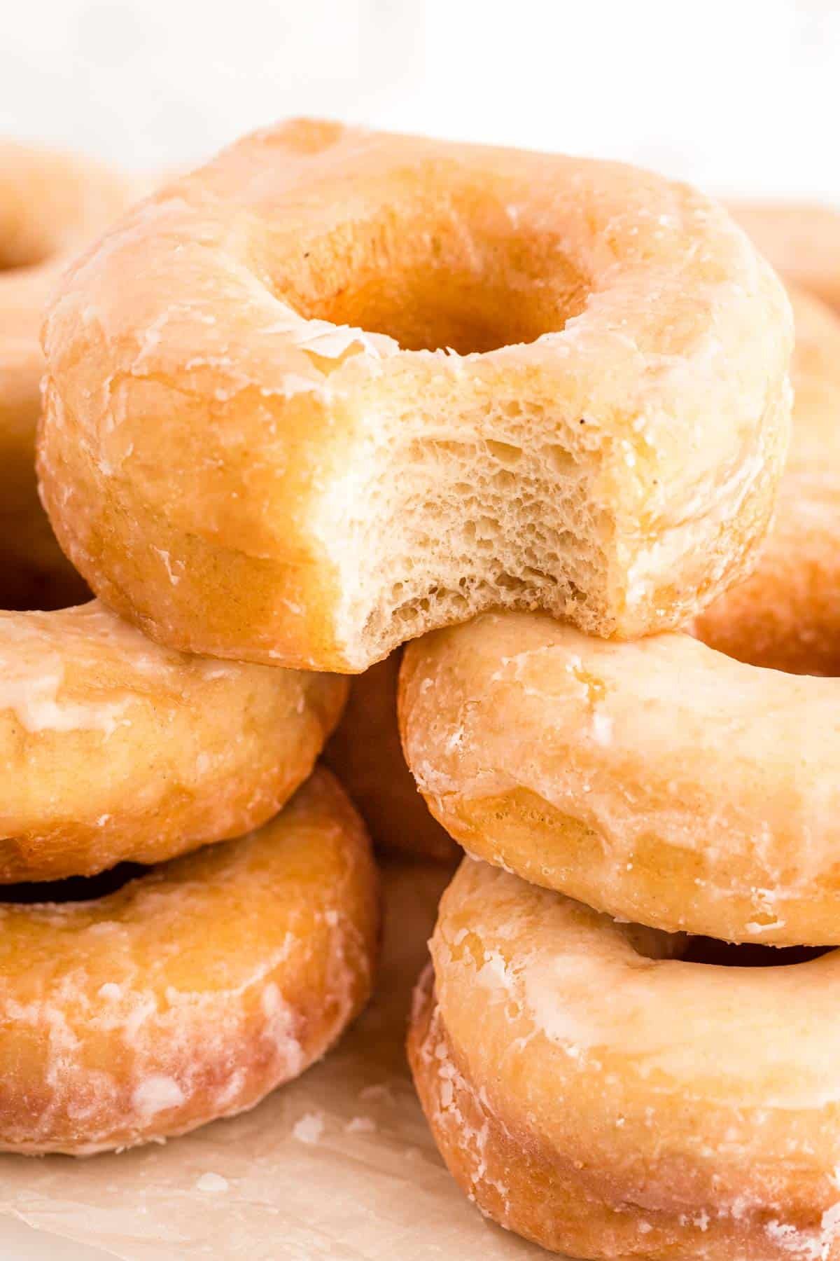 Close up photo of sourdough donuts piled on a cutting board, the top one is missing a bite.