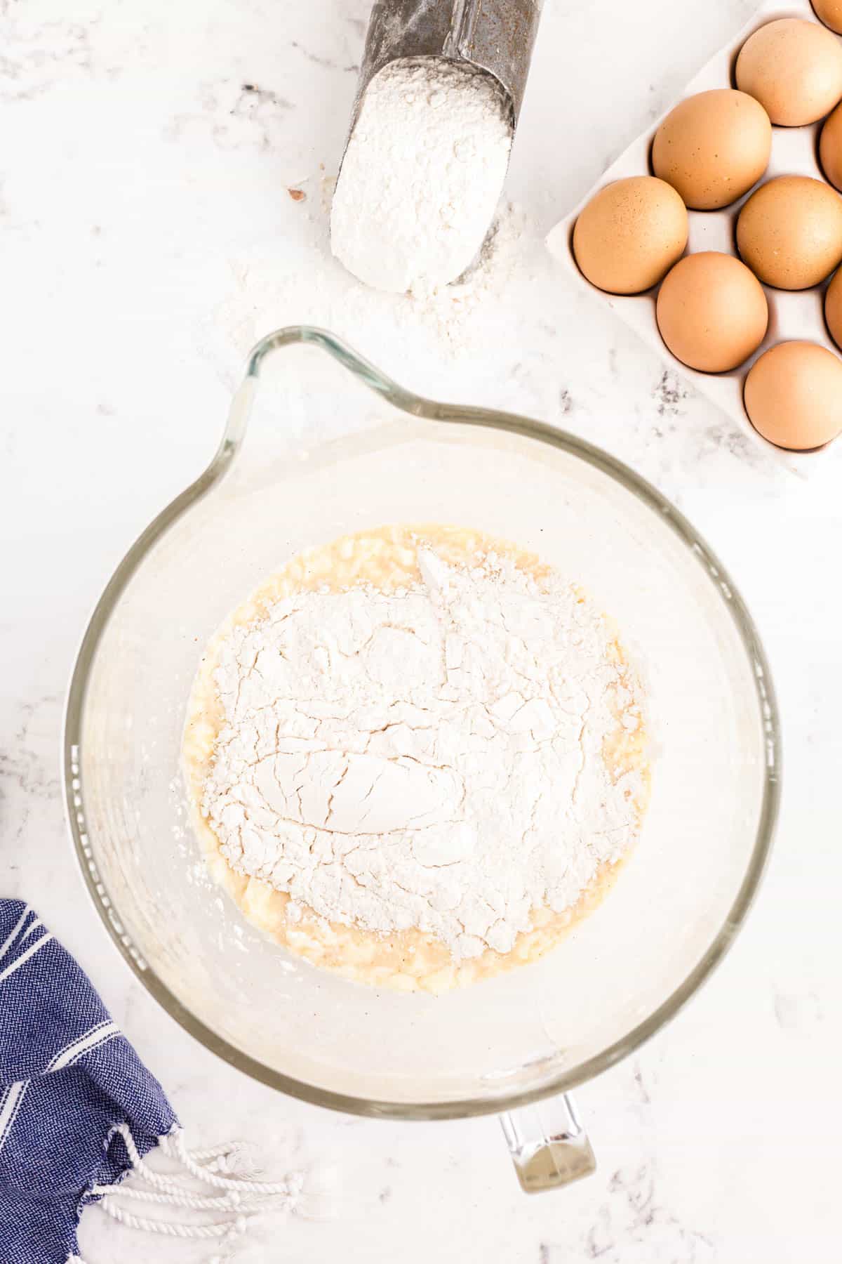 Flour being added to a glass mixing bowl to make donut dough.