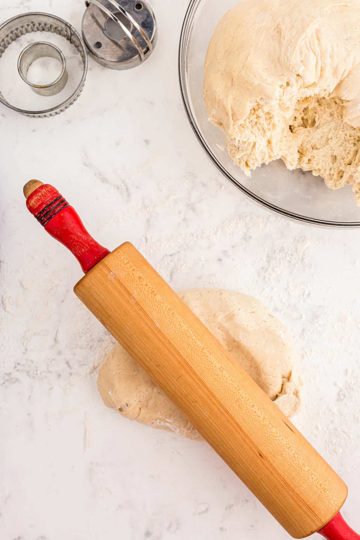 Donut dough being rolled out with a rolling pin.