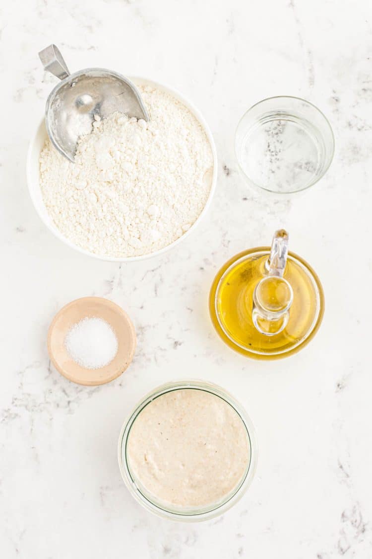 Ingredients to make sourdough pizza crust on a marble counter.