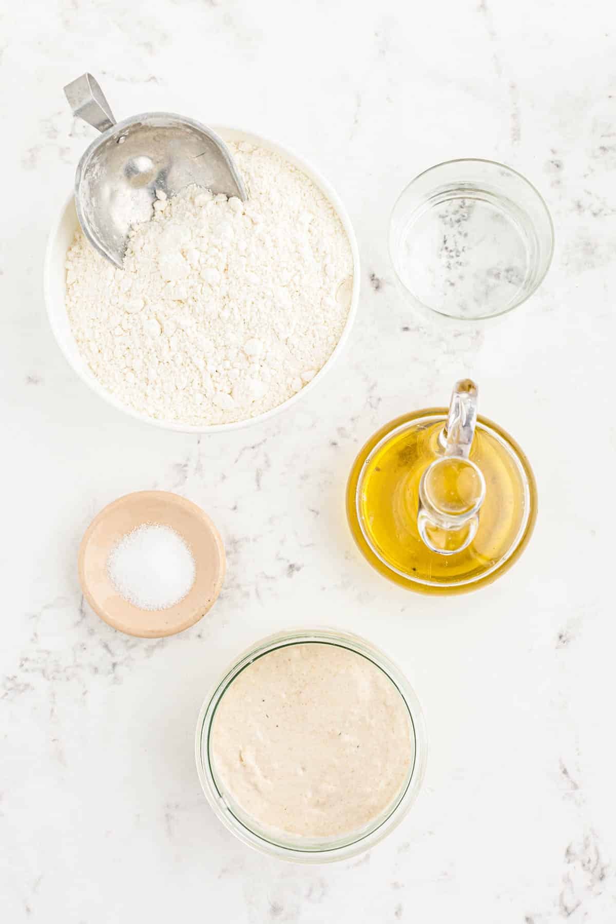 Ingredients to make sourdough pizza crust on a marble counter.