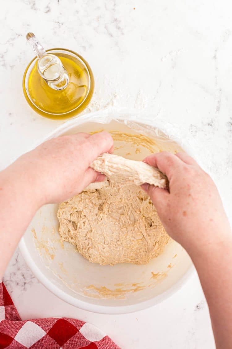 Soudough pizza dough being stretched and folded in a bowl.