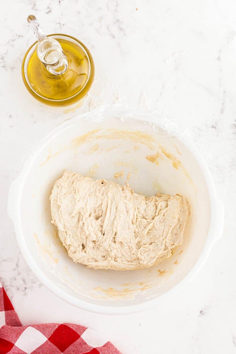 Sourdough pizza crust dough folded over in a white bowl.