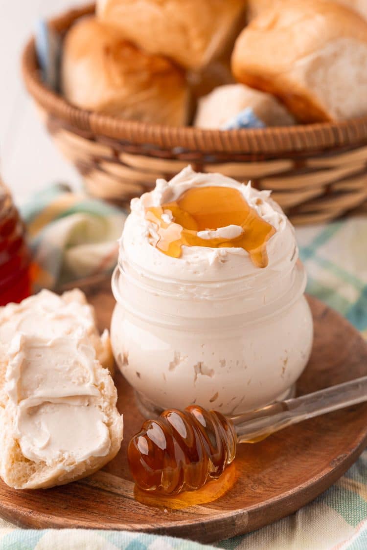 A jar filled with whipped honey butter on a wooden plate.