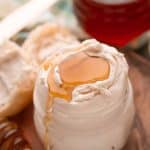 Honey butter in a glass jar on a wooden plate with a roll next to it.