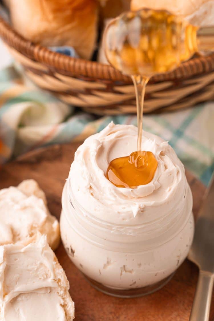 Honey being drizzled on top of a jar of whipped honey butter.